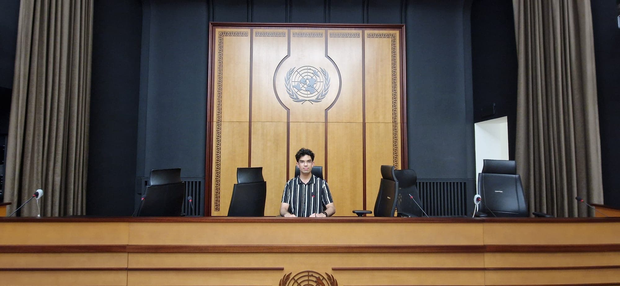 Seated at the rostrum of an assembly hall beneath the United Nations emblem